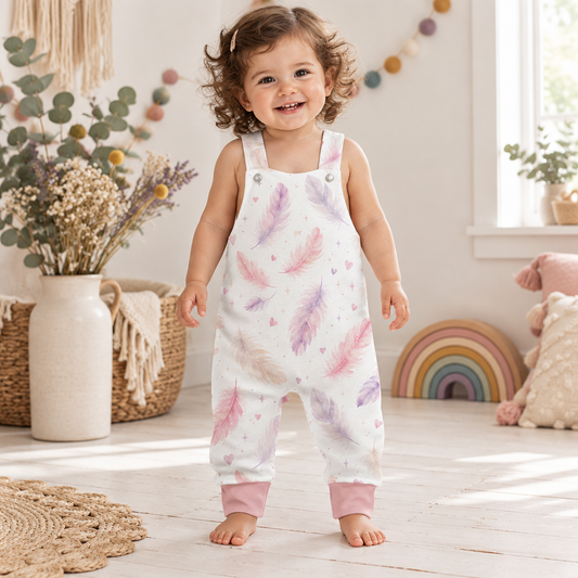 Kind trägt die helle Latzhose mit zarten Federn in Rosa und Flieder