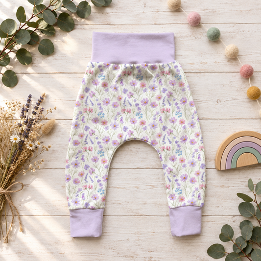 Pumphose mit zartem Wildblumenmuster, fliederfarbenem Bauchbund und passenden Bündchen als dekoriertes Flatlay.